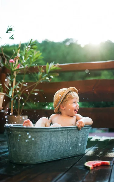 Kleiner Junge mit Hut in der Badewanne im Garten im Sommer, isst Wassermelone. — Stockfoto