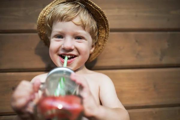Egy kisfiú, nyáron a teraszon fából készült háttér ital állandó. — Stock Fotó