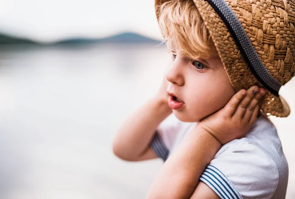 A close-up of small toddler boy standing outdoors in summer, holding a hat. — Stock Photo, Image