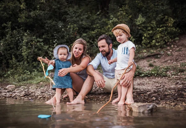 Mladá rodina se dvěma dětmi batole venku u řeky v létě. — Stock fotografie