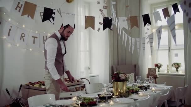 Giovane uomo con fiocco e gilet apparecchiare una tavola per una festa al coperto . — Video Stock