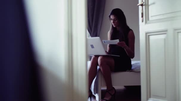 Ung affärskvinna på affärsresa sitter i ett hotellrum, med laptop. — Stockvideo