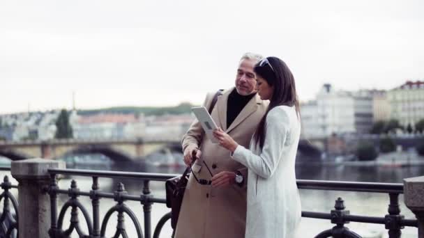 Man en vrouw business partners met tablet staan door een rivier in het centrum van Praag. — Stockvideo