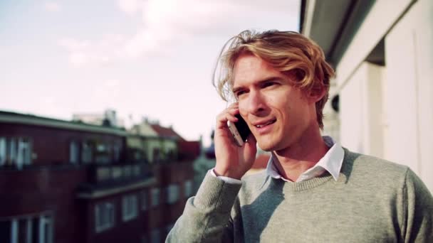 Νέος άνθρωπος με smartphone στέκεται σε ένα μπαλκόνι στην πόλη, κάνοντας ένα τηλεφώνημα. — Αρχείο Βίντεο