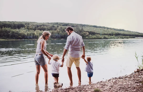 Eine Rückansicht einer Familie mit zwei Kleinkindern im Sommer im Freien am Fluss. — Stockfoto