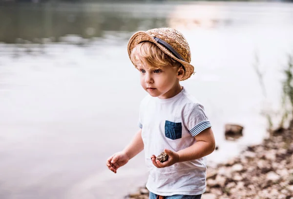 Malé batole chlapec stojící venku u řeky v létě, hraje. — Stock fotografie