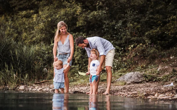 Молодая семья с двумя маленькими детьми на открытом воздухе у реки летом, играя. — стоковое фото