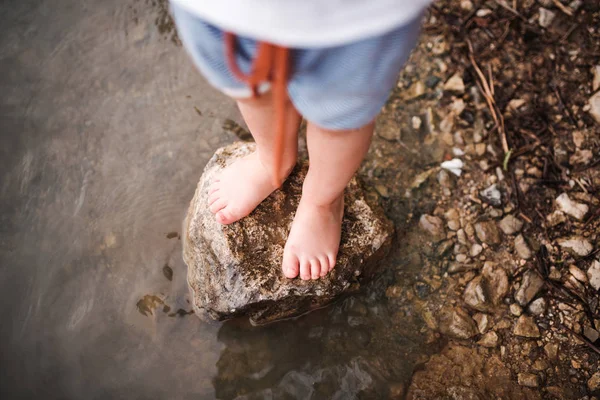 Ein mittlerer Teil eines kleinen Jungen, der im Sommer draußen an einem Fluss steht. Ansicht von oben. — Stockfoto