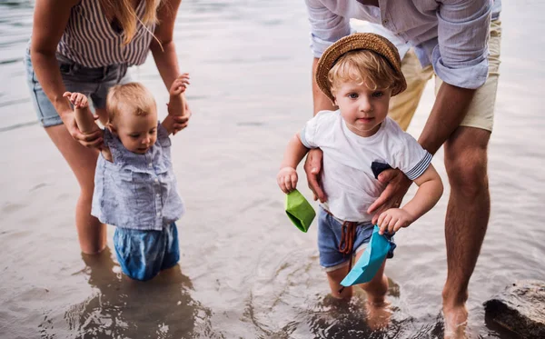 Una sección media de la familia con dos niños pequeños al aire libre junto al río en verano . —  Fotos de Stock