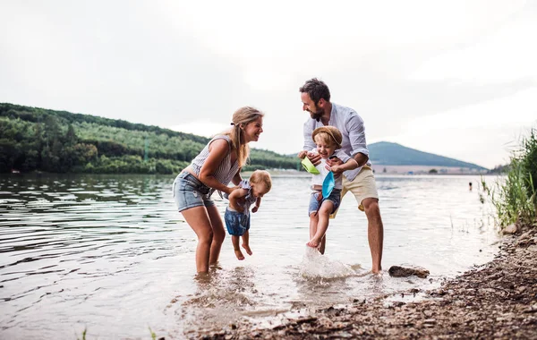 Una familia joven con dos niños pequeños al aire libre junto al río en verano . — Foto de Stock