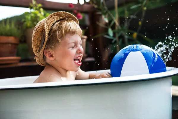 Piccolo ragazzo con una palla in bagno all'aperto in giardino in estate, giocando in acqua . — Foto Stock