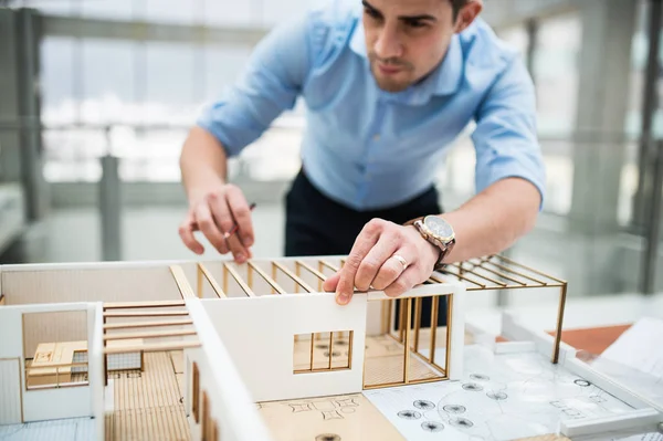 Ung affärsman eller arkitekt med modell av ett hus stående på kontoret, arbetar. — Stockfoto