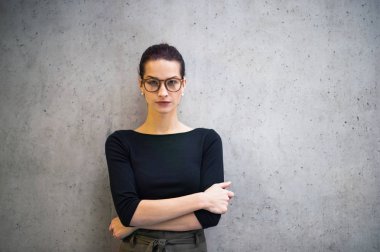 Ofiste ayakta, kameraya bakarak gözlüklü genç işkadını portresi.