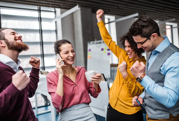 Un grupo de jóvenes empresarios con smartphone de pie en la oficina, expresando emoción . — Foto de Stock