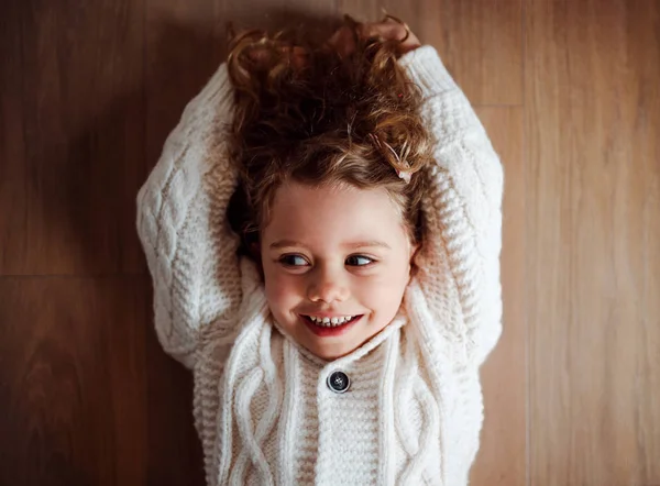 Ein Porträt eines kleinen Mädchens mit weißem Strickpullover auf dem Boden liegend, eine Draufsicht. — Stockfoto