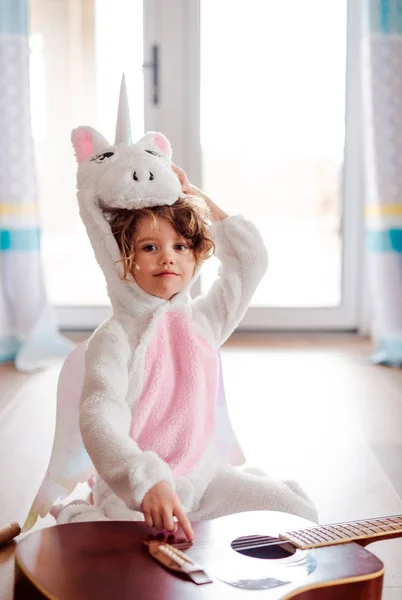 Un retrato de niña pequeña en máscara de unicornio con guitarra en casa . — Foto de Stock