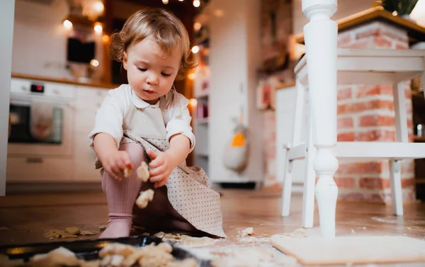 Een kleine peuter meisje het maken van taarten op de vloer in de keuken thuis. — Stockfoto