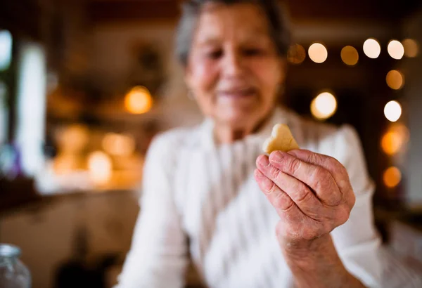 A close-up of elderly woman making cakes in a kitchen at home, holding a biscuit. — Stock Photo, Image