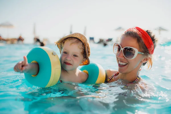 Un niño pequeño con brazaletes y madre nadando en el agua en las vacaciones de verano . — Foto de Stock