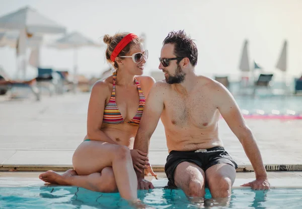 Um casal de maiô sentado à beira da piscina nas férias de verão . — Fotografia de Stock