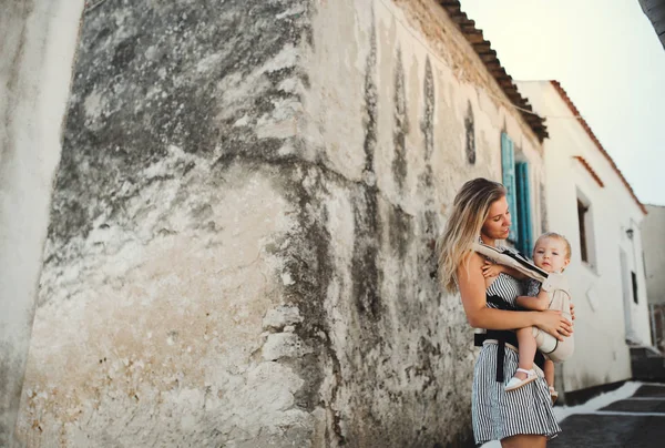 Een jonge moeder met een baby in een vervoerder lopen in de stad op zomervakantie. — Stockfoto