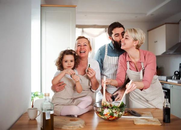 En liten flicka med föräldrar och mormor hemma, förbereda grönsakssallad. — Stockfoto