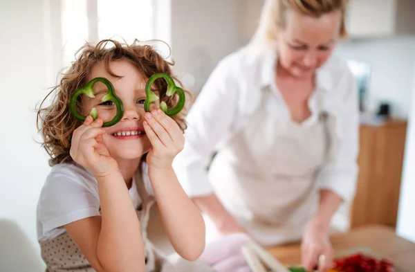 Un retrato de niña pequeña con la abuela preparando ensalada de verduras en casa, divirtiéndose . —  Fotos de Stock