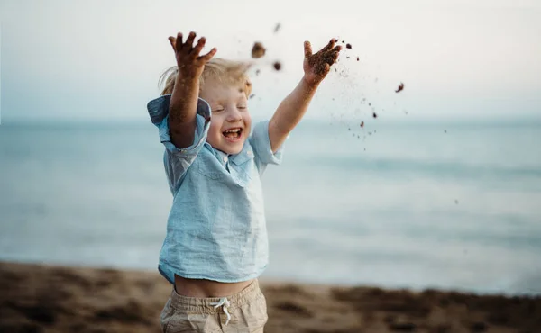 Ein kleiner Junge steht im Sommerurlaub am Strand und wirft Sand. — Stockfoto