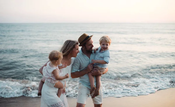 Mladá rodina se dvěma dětmi batole stojící na pláži o letních prázdninách. — Stock fotografie