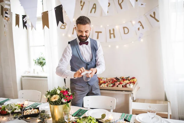 弓と屋内のパーティーのためのテーブルの設定のベストと中年の男性. — ストック写真