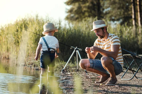 Ein reifer Vater mit einem kleinen Sohn im Freien beim Angeln an einem See. — Stockfoto