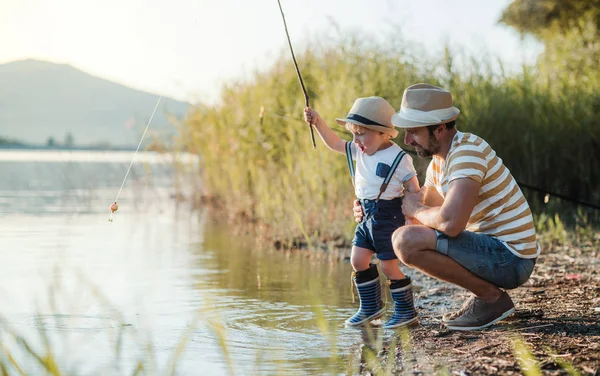 Un padre maduro con un pequeño hijo pequeño al aire libre pesca junto a un lago . —  Fotos de Stock