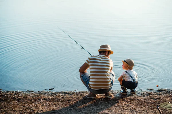 Eine Rückansicht eines erwachsenen Vaters mit einem kleinen Sohn im Freien beim Angeln an einem See. — Stockfoto