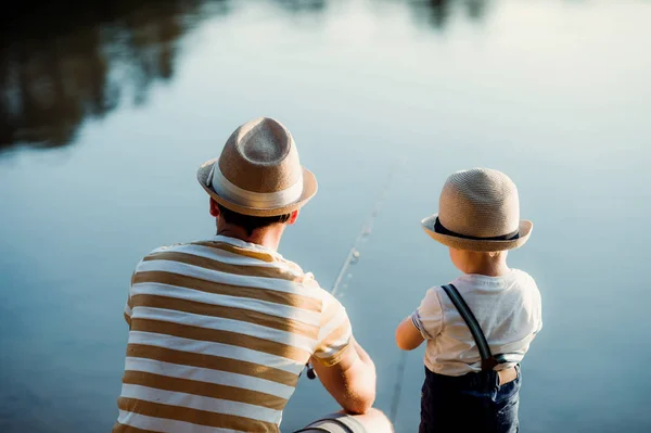 Eine Rückansicht eines erwachsenen Vaters mit einem kleinen Sohn im Freien beim Angeln an einem See. — Stockfoto