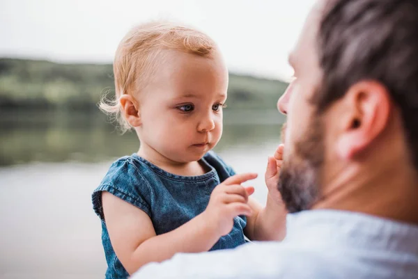 Un padre con una bambina all'aperto vicino al fiume in estate . — Foto Stock