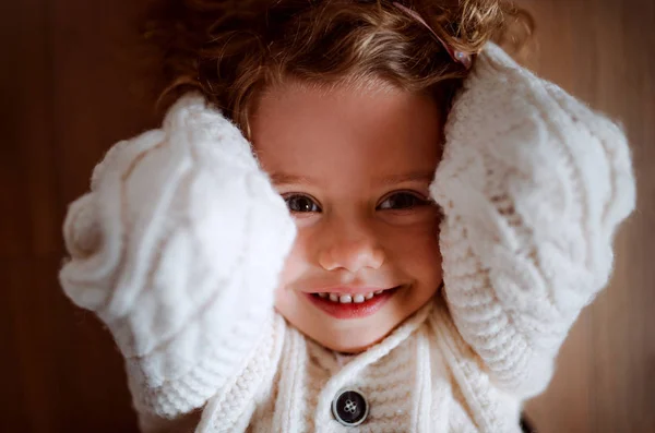 Ein Porträt eines kleinen Mädchens mit weißem Strickpullover auf dem Boden liegend, eine Draufsicht. — Stockfoto