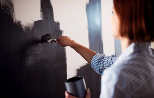 Uma jovem mulher pintando parede preta. Uma startup de pequenas empresas . — Fotografia de Stock