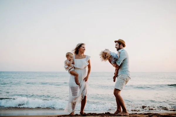 Una familia joven con dos niños pequeños de pie en la playa en las vacaciones de verano . —  Fotos de Stock