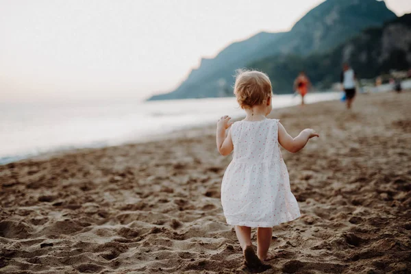มุมมองด้านหลังของเด็กผู้หญิงตัวเล็ก ๆ เดินบนชายหาดในวันหยุดฤดูร้อน . — ภาพถ่ายสต็อก