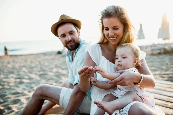 Una familia con una niña pequeña sentada en la playa de arena en las vacaciones de verano . —  Fotos de Stock