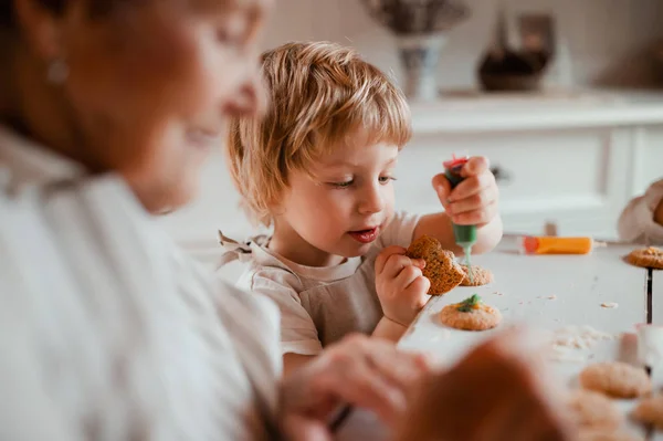 Una abuela mayor con un niño pequeño haciendo pasteles en casa . —  Fotos de Stock