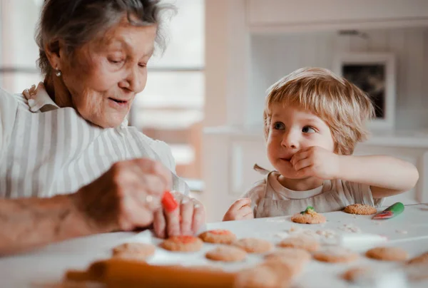 Una nonna anziana con il piccolo bambino che fa torte a casa . — Foto Stock