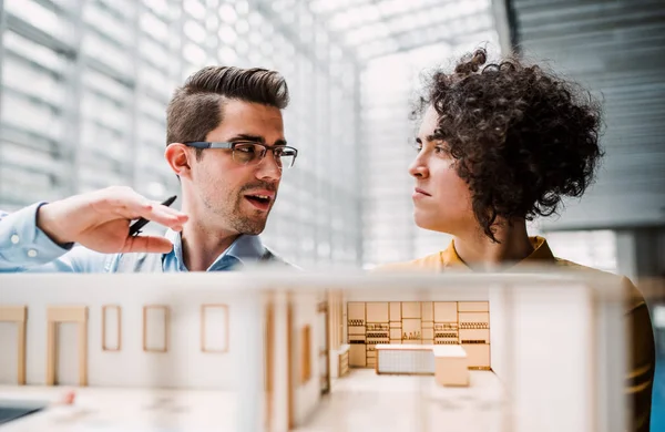 Young architects with model of a house standing in office, talking. — Stock Photo, Image