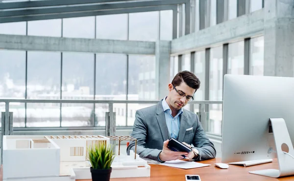 Giovane uomo d'affari o architetto con modello di una casa seduta in ufficio, al lavoro . — Foto Stock
