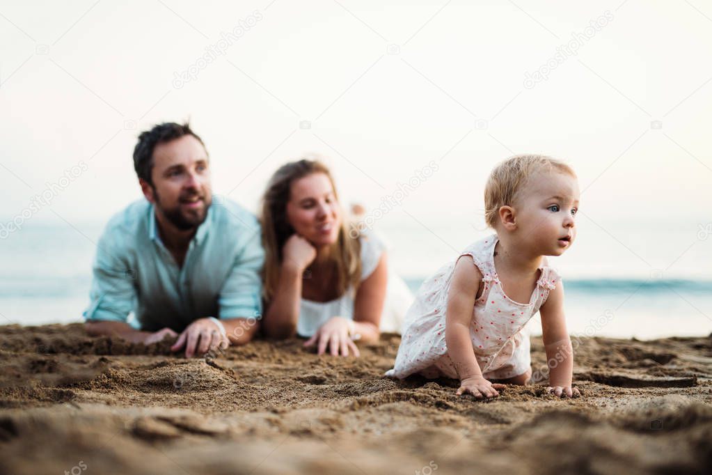 A family with a toddler girl lying on sand beach on summer holiday.