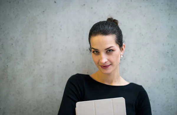 Jonge zakenvrouw met tablet staan tegen een betonnen muur in kantoor. — Stockfoto