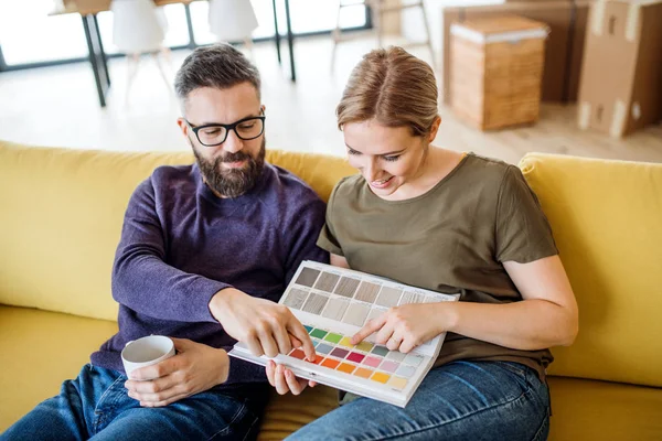 Una joven pareja con muestras de color sentada en el sofá, mudándose en un nuevo hogar . — Foto de Stock