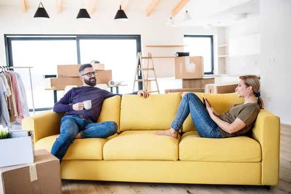 A young couple with tablet and coffee sitting on sofa, moving in new home. — Stock Photo, Image