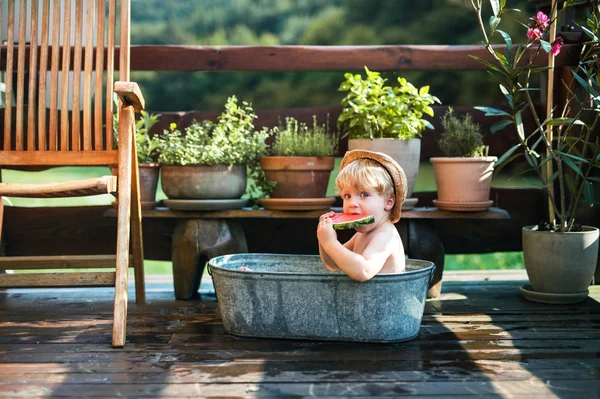 Niño pequeño con un sombrero en el baño al aire libre en el jardín en verano, comiendo sandía . — Foto de Stock