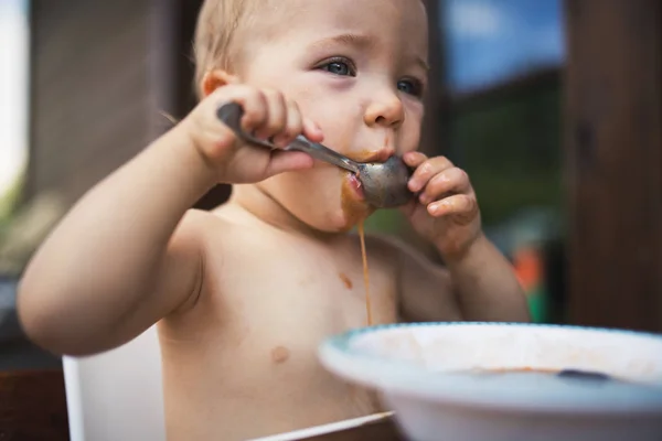 Niña de pie junto a una mesa en un patio en verano, comiendo sopa . —  Fotos de Stock